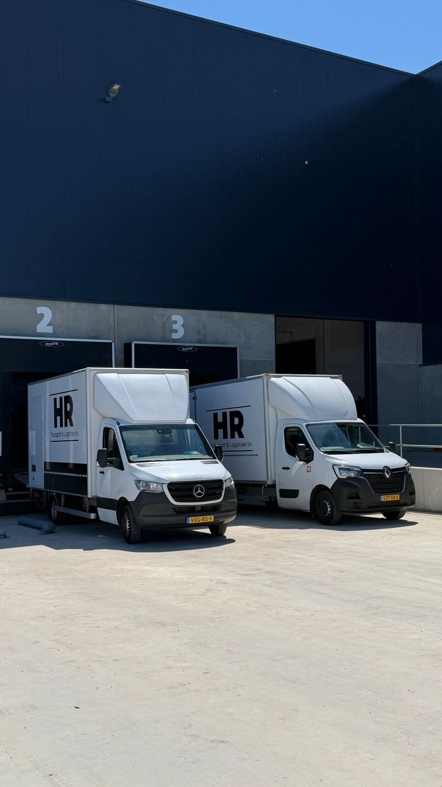 Twee bakwagens van HR Transport & Logistiek bij de laaddocks van een distributiecentrum